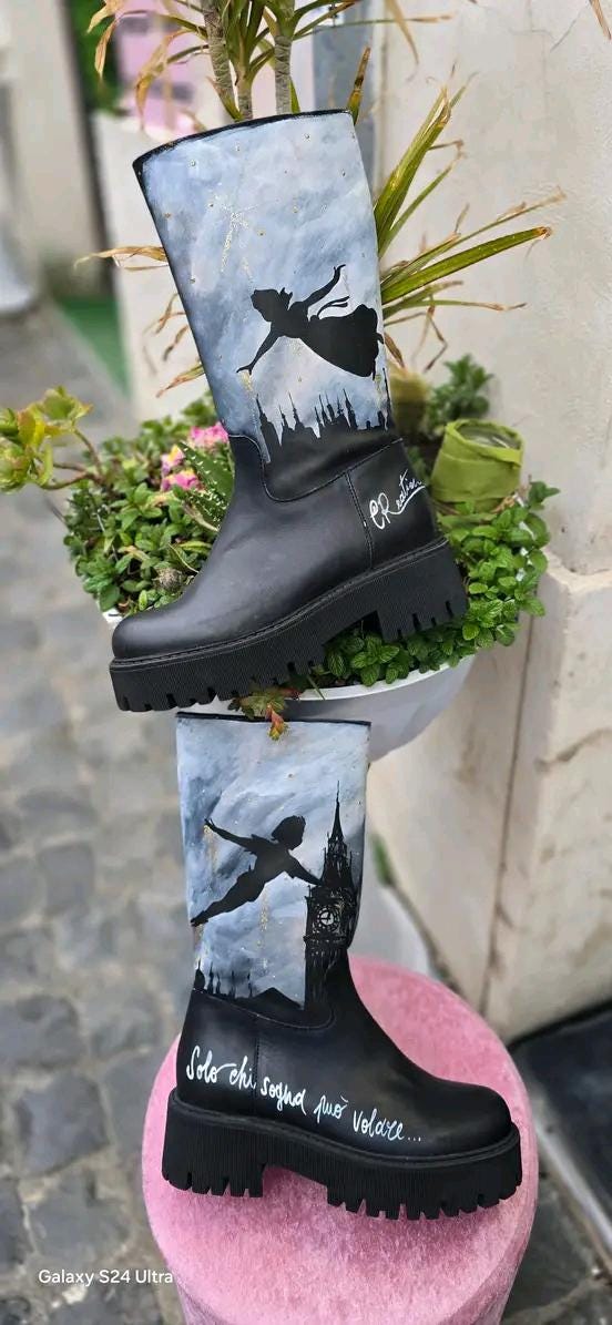 Stivale Dipinto a Mano con Personaggi di Peter Pan - Solo chi sogna può volare + Promo Stivale + Borsa Coordinata Aggiungi un tocco di magia al tuo look con questi stivali dipinti a mano, ispirati al mondo incantato di Peter Pan! Ogni paio è realizzato con cura e dettagli, con due personaggi di Peter Pan che volano nel cielo, accompagnati da uno sfondo mozzafiato. La frase "Solo chi sogna può volare" rende questo prodotto ancora più speciale, perfetto per chi ama sognare e vivere ogni giorno come una nuova