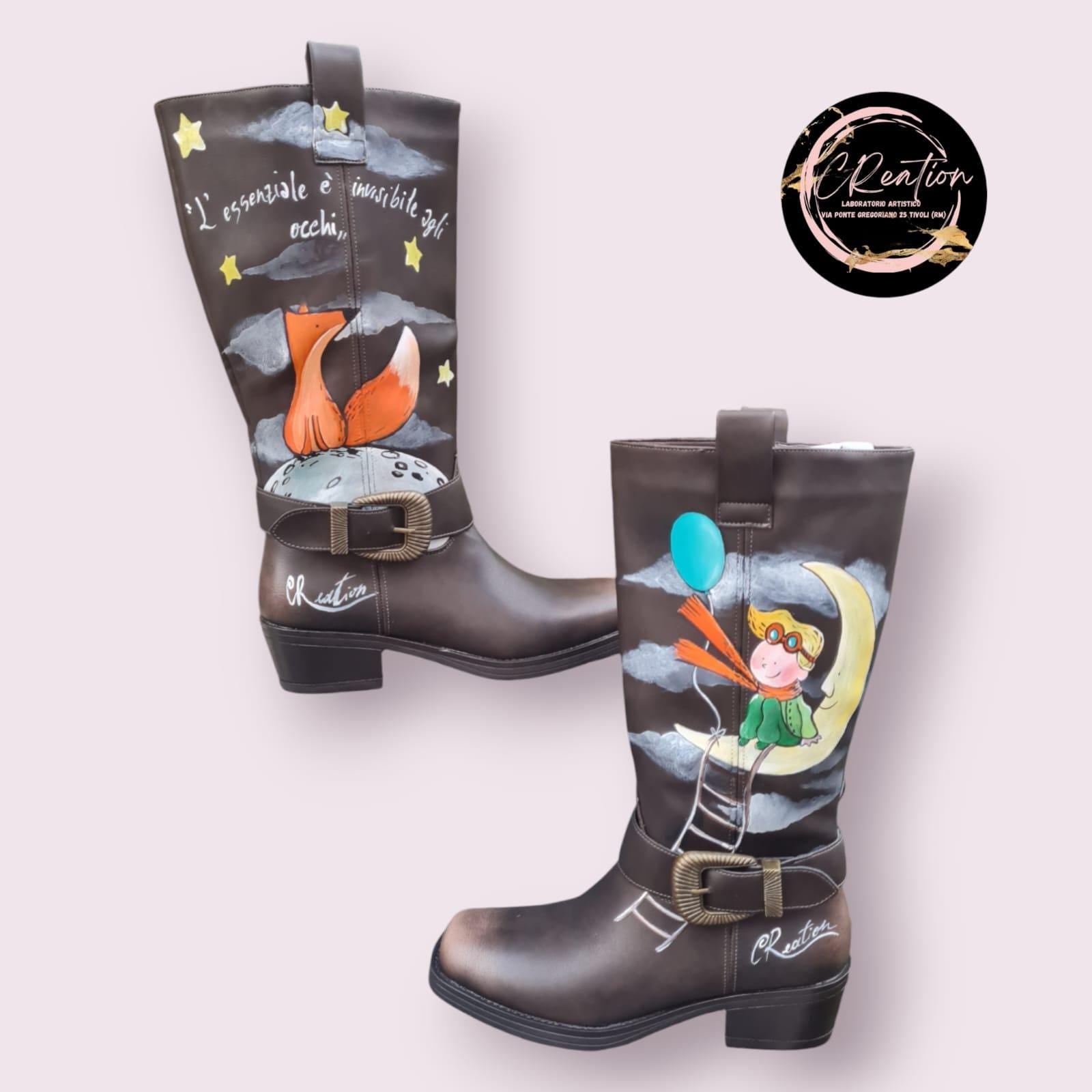 Stivali dipinti a mano - Il Piccolo Principe 🧩 *Coordinabile su richiesta:* È possibile ordinare *un portafoglio , una borsa o un giacchetto perfettamente abbinato* con lo stesso stile e soggetto ! Porta con te la magia del Piccolo Principe con questi stivali unici, dipinti a mano con cura e passione. Il design raffigura il piccolo principe seduto su una luna, mentre la sua fidata amica, la volpe, è disegnata su un pianeta lontano