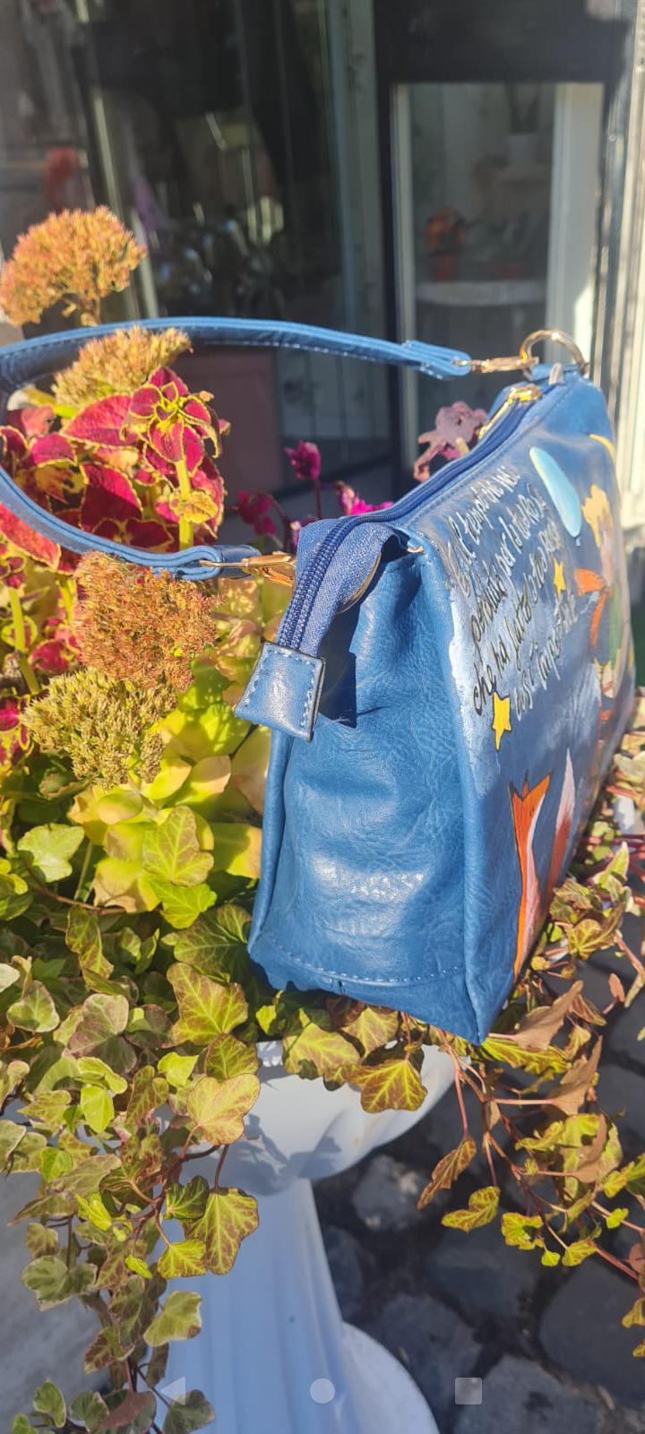 Borsa Dipinta a Mano - Il Piccolo Principe | Accessorio Unico e Magico Porta con te un pezzo di magia e saggezza con questa borsa dipinta a mano, che celebra il Piccolo Principe, il celebre personaggio creato da Antoine de Saint-Exupéry. Ogni borsa è realizzata con amore, utilizzando colori acrilici di alta qualità, per un design unico che racconta una storia di avventura, sogni e riflessioni. 🧩 *Coordinabile su richiesta:* È possibile ordinare *un portafoglio o un giacchetto perfettamente abbinato* con lo