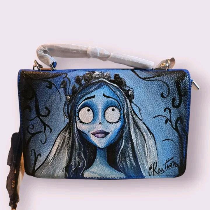 *Borsa Dipinta a Mano – Sposa Cadavere 💀🌹* Porta con te un po' di *magia gotica* e *romanticismo oscuro* con questa *borsa dipinta a mano* ispirata alla celebre *Sposa Cadavere*! 🎨✨ Ogni borsa è realizzata con *colori acrilici di alta qualità* su *ecopelle resistente*, immortalando la figura di Emily in tutto il suo misterioso fascino. Perfetta per gli amanti del *film di Tim Burton*, questa borsa unisce arte e stile gotico in un accessorio unico! 🖤 🧩 *Coordinabile su richiesta:* È possibile ordinare *