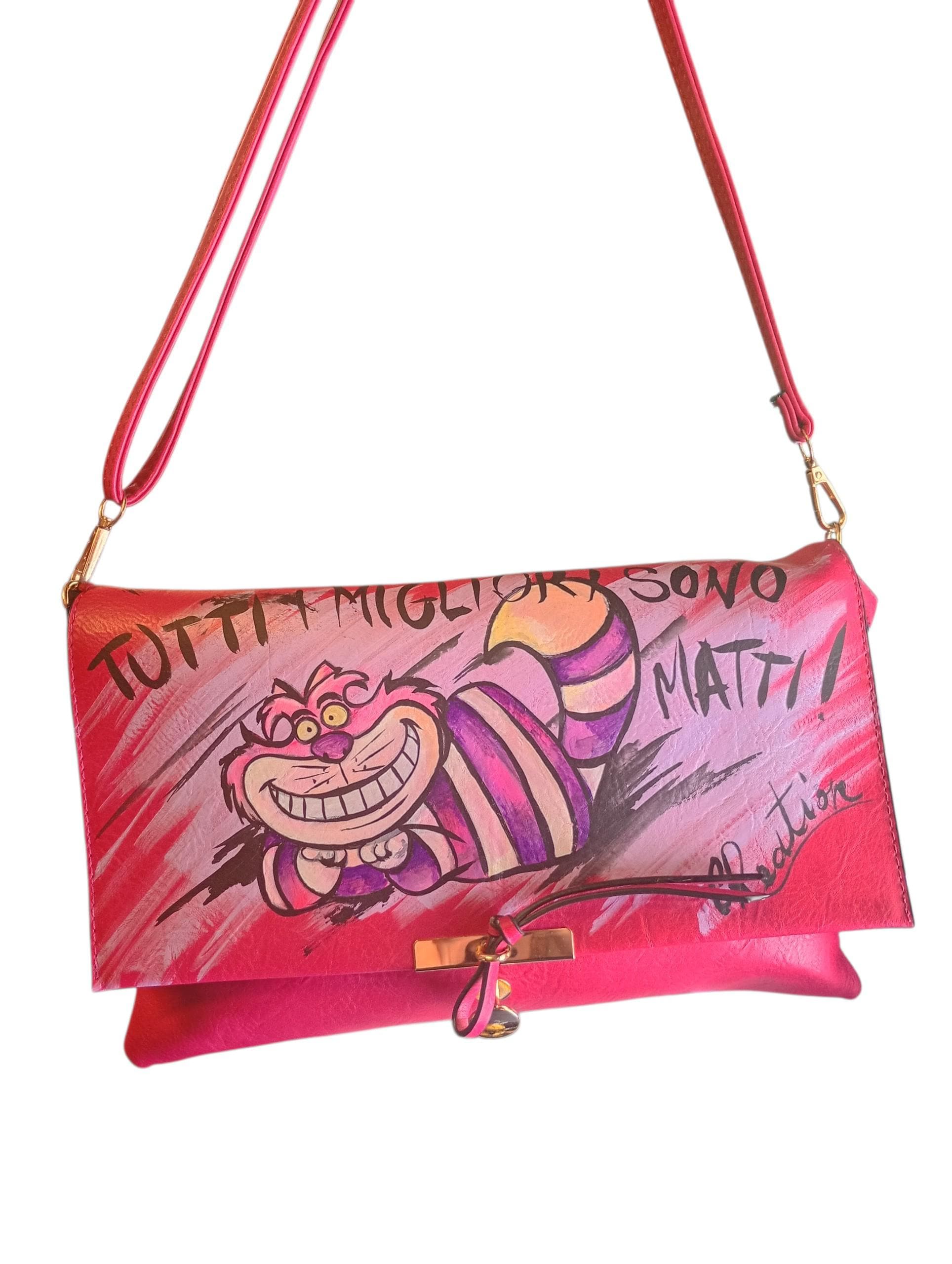 Porta sempre con te la magia, il mistero e la follia del gatto più famoso del Paese delle Meraviglie. Questa borsa dipinta a mano celebra l'universo dello Stregatto, unendo un accessorio pratico e di tendenza all'esclusività di un prodotto interamente artigianale, arricchito dalla celebre frase "Tutti i migliori sono matti".
Realizzata con colori professionali specifici per tessuti, è perfetta per gli amanti delle favole, dei libri fantasy e per chiunque cerchi un tocco di originalità e un pizzico di sana f