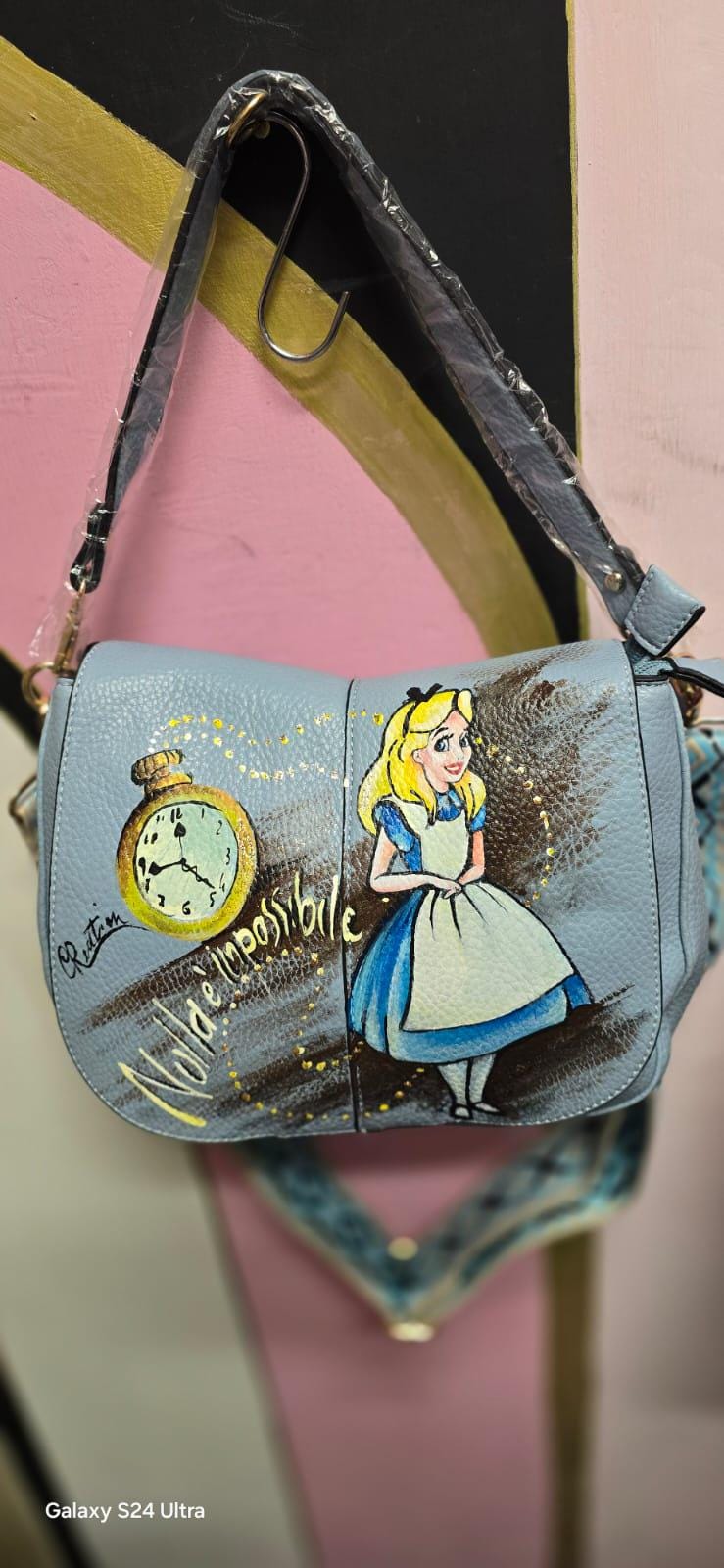 Borsa dipinta a mano "Alice nel Paese delle Meraviglie" - Scritta "Nulla è impossibile" Questa borsa in ecopelle è un'opera unica, realizzata interamente a mano con colori acrilici di alta qualità. Il design rappresenta un omaggio al classico "Alice nel Paese delle Meraviglie", con l'aggiunta della frase "Nulla è impossibile", che conferisce un tocco di magia e ispirazione a ogni outfit. 🧩 *Coordinabile su richiesta:*