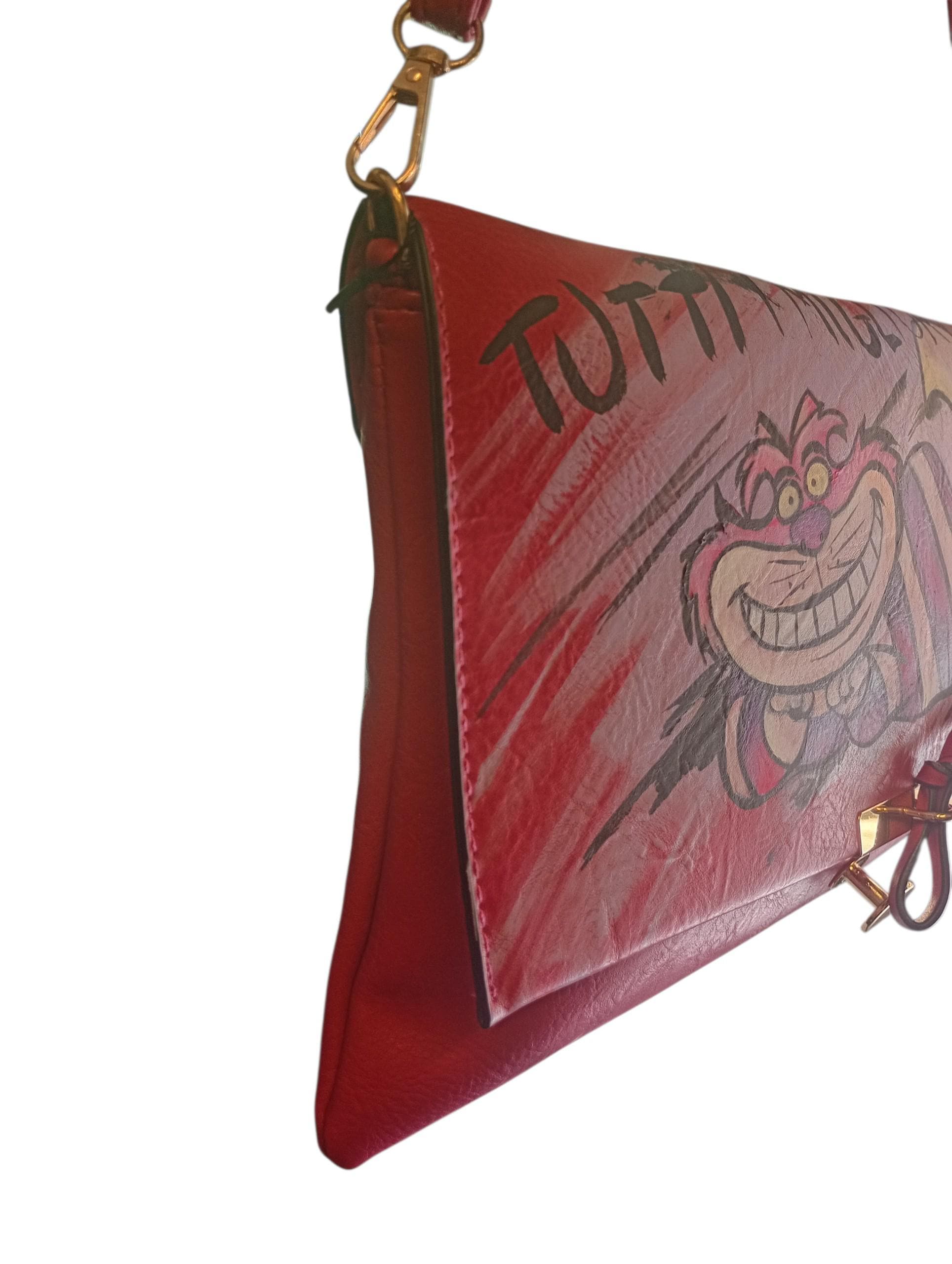 Porta sempre con te la magia, il mistero e la follia del gatto più famoso del Paese delle Meraviglie. Questa borsa dipinta a mano celebra l'universo dello Stregatto, unendo un accessorio pratico e di tendenza all'esclusività di un prodotto interamente artigianale, arricchito dalla celebre frase "Tutti i migliori sono matti".
Realizzata con colori professionali specifici per tessuti, è perfetta per gli amanti delle favole, dei libri fantasy e per chiunque cerchi un tocco di originalità e un pizzico di sana f