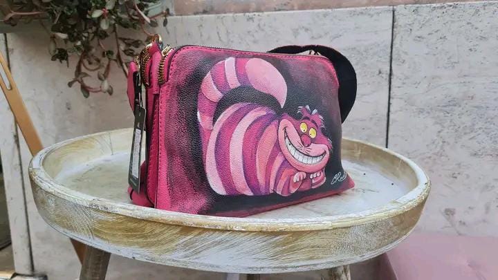 "Borsa Stregatto Alice nel Paese delle Meraviglie in Ecopelle | Dipinta a Mano | Lavabile fino a 40°C" 🧩 *Coordinabile su richiesta:* È possibile ordinare *un portafoglio o un giacchetto perfettamente abbinato* con lo stesso stile e soggetto ! Descrizione: Questa borsa unica nel suo genere è ispirata al famoso Stregatto di "Alice nel Paese delle Meraviglie".