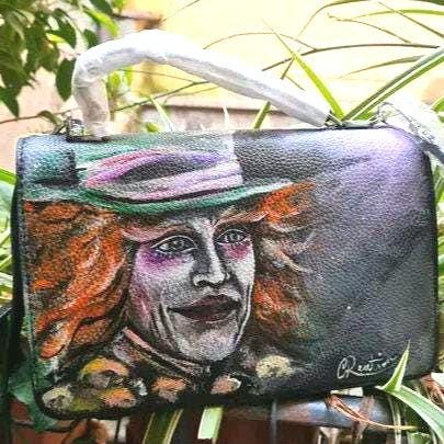 Borsa Dipinta a Mano - Il Cappellaio Matto | Alice nel Paese delle Meraviglie | Accessorio Unico ✨ Un tocco di follia e magia per il tuo stile! ✨ Questa borsa unica è dipinta a mano con colori acrilici resistenti e raffigura il Cappellaio Matto, uno dei personaggi più iconici e stravaganti di Alice nel Paese delle Meraviglie! Un accessorio perfetto per gli amanti del mondo Disney e per chi vuole aggiungere un tocco di originalità e fantasia ai propri outfit