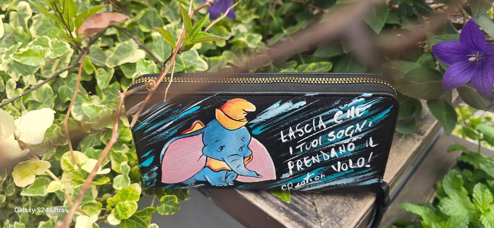 *Portafoglio Dipinto a Mano – Dumbo &amp; Frase Motivazionale 🎨🐘* Un accessorio unico che unisce dolcezza e ispirazione! Questo portafoglio in ecopelle è dipinto a mano con colori acrilici professionali e ha come protagonista *Dumbo*, il tenero elefantino del celebre cartone Disney, accompagnato dalla frase: *"Lascia che i tuoi sogni prendano il volo"* ✨ 🖌️ *Dettagli del prodotto*: - Materiale: Ecopelle - Tecnica: Dipinto a mano con colori acrilici sigillati - Lavabile a mano o in lavatrice fino a 40° - 