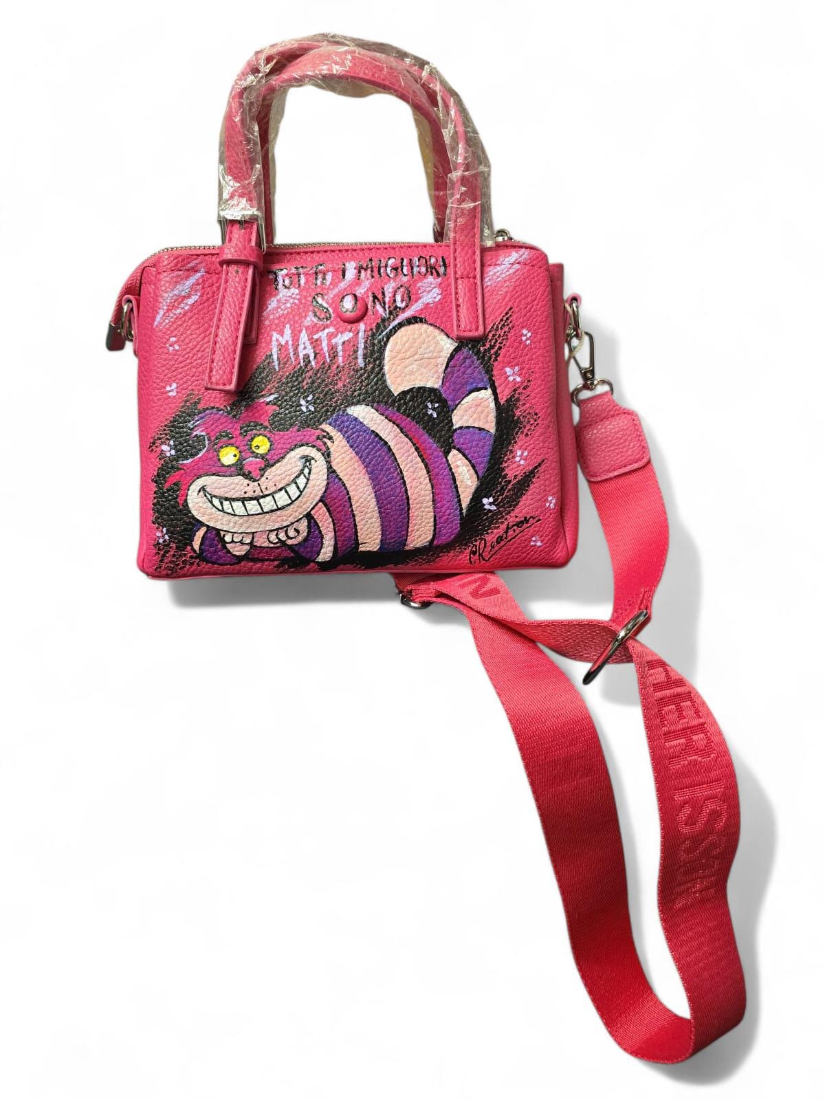 Borsa dipinta a mano – Stregatto + frase “Tutti i migliori sono matti” – Unica e personalizzabile *Descrizione:* 🎨 Borsa artigianale dipinta interamente a mano, realizzata in *pelle o ecopelle di alta qualità* e decorata con *colori acrilici professionali*, resistenti all'acqua e all'usura. Il soggetto principale è lo *Stregatto*, iconico personaggio di “Alice nel Paese delle Meraviglie”, accompagnato dalla frase *“Tutti i migliori sono matti”*, perfetta per chi ama distinguersi con stile e creatività!