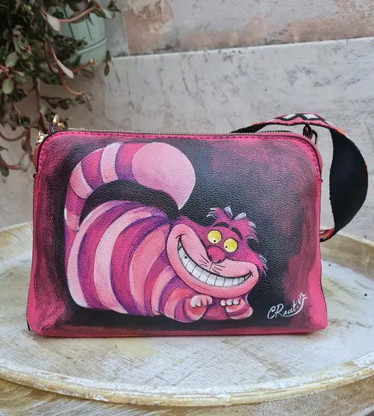"Borsa Stregatto Alice nel Paese delle Meraviglie in Ecopelle | Dipinta a Mano | Lavabile fino a 40°C" 🧩 *Coordinabile su richiesta:* È possibile ordinare *un portafoglio o un giacchetto perfettamente abbinato* con lo stesso stile e soggetto ! Descrizione: Questa borsa unica nel suo genere è ispirata al famoso Stregatto di "Alice nel Paese delle Meraviglie".