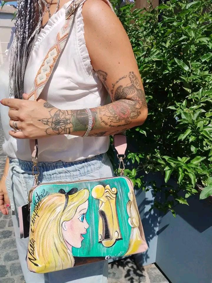 Borsa Dipinta a Mano - Alice nel Paese delle Meraviglie | Accessorio Unico e Magico ✨ Un tocco di fantasia e meraviglia per il tuo stile! ✨ Questa borsa unica è dipinta a mano con colori acrilici resistenti e raffigura Alice nel Paese delle Meraviglie, uno dei personaggi più amati e sognanti della letteratura e del mondo Disney. Un accessorio perfetto per chi ama le fiabe, l’arte e gli oggetti unici fatti a mano.