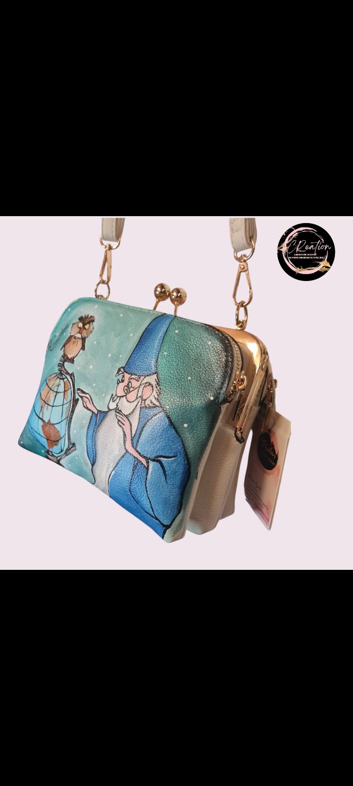 Mago Merlino della Spada nella Roccia borsa dipinta a mano Descrizione: Porta un po' di magia nella tua vita con questa borsa dipinta a mano, che celebra il leggendario Mago Merlino della Spada nella Roccia! Un accessorio unico, realizzato artigianalmente, che ti farà sentire come se fossi tu il protagonista di una storia magica. Perfetta per ogni fan Disney, questa borsa è un pezzo esclusivo e irripetibile che aggiungerà un tocco di fantasia al tuo look