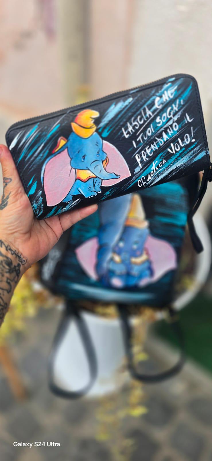 *Portafoglio Dipinto a Mano – Dumbo &amp; Frase Motivazionale 🎨🐘* Un accessorio unico che unisce dolcezza e ispirazione! Questo portafoglio in ecopelle è dipinto a mano con colori acrilici professionali e ha come protagonista *Dumbo*, il tenero elefantino del celebre cartone Disney, accompagnato dalla frase: *"Lascia che i tuoi sogni prendano il volo"* ✨ 🖌️ *Dettagli del prodotto*: - Materiale: Ecopelle - Tecnica: Dipinto a mano con colori acrilici sigillati - Lavabile a mano o in lavatrice fino a 40° - 