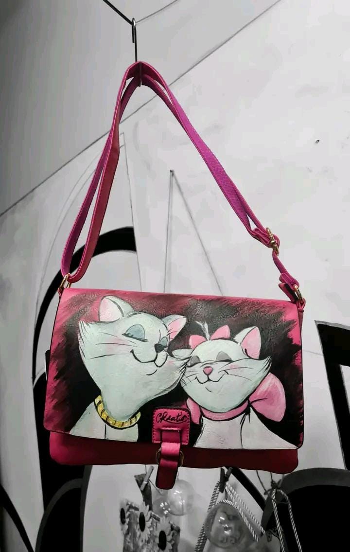 Borsa Dipinta a Mano con Personaggi degli Aristogatti - Borsa Unica in Ecopelle, Personalizzabile, Regalo Originale Descrizione: Questa borsa dipinta a mano è ispirata ai celebri personaggi del cartone animato Gli Aristogatti. Realizzata in ecopelle di alta qualità, la borsa presenta un'illustrazione unica che raffigura i simpatici gatti protagonisti. La pittura è realizzata con colori acrilici, che garantiscono una lunga durata e un aspetto vibrante