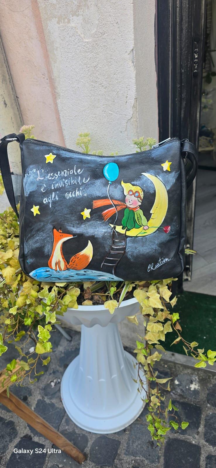 *Borsa dipinta a mano – Il Piccolo Principe e la Volpe* 🌙🦊 Citazione: “L’essenziale è invisibile agli occhi” 🧩 *Coordinabile su richiesta:* È possibile ordinare *un portafoglio o un giacchetto perfettamente abbinato* con lo stesso stile e soggetto ! Borsa in ecopelle nera dipinta interamente a mano con il dolcissimo tema de *Il Piccolo Principe*, protagonista sulla luna con la volpe e una pioggia di stelle. Un pezzo unico e poetico, perfetto per chi ama distinguersi con stile e significato