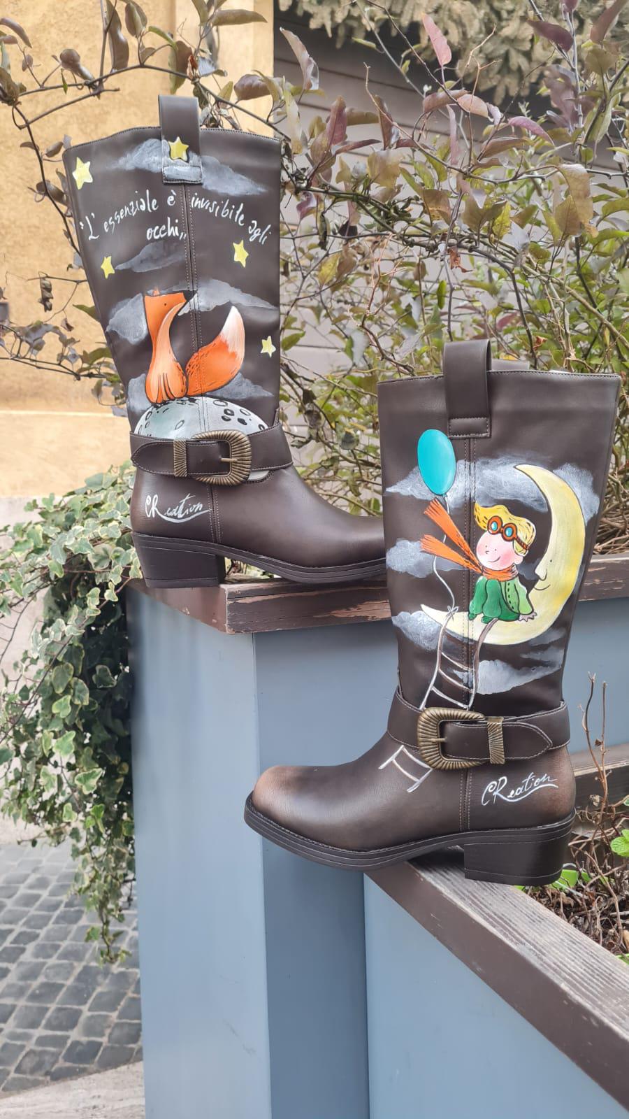 Stivali dipinti a mano - Il Piccolo Principe 🧩 *Coordinabile su richiesta:* È possibile ordinare *un portafoglio , una borsa o un giacchetto perfettamente abbinato* con lo stesso stile e soggetto ! Porta con te la magia del Piccolo Principe con questi stivali unici, dipinti a mano con cura e passione. Il design raffigura il piccolo principe seduto su una luna, mentre la sua fidata amica, la volpe, è disegnata su un pianeta lontano