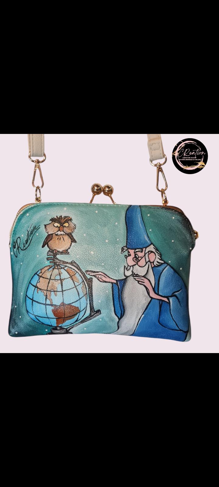 Mago Merlino della Spada nella Roccia borsa dipinta a mano Descrizione: Porta un po' di magia nella tua vita con questa borsa dipinta a mano, che celebra il leggendario Mago Merlino della Spada nella Roccia! Un accessorio unico, realizzato artigianalmente, che ti farà sentire come se fossi tu il protagonista di una storia magica. Perfetta per ogni fan Disney, questa borsa è un pezzo esclusivo e irripetibile che aggiungerà un tocco di fantasia al tuo look